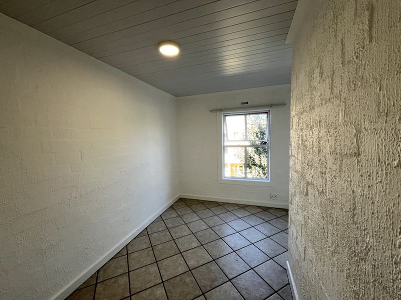 An empty bedroom featuring tiled flooring, textured brick walls, and a tongue and groove ceiling with a single window providing natural light.