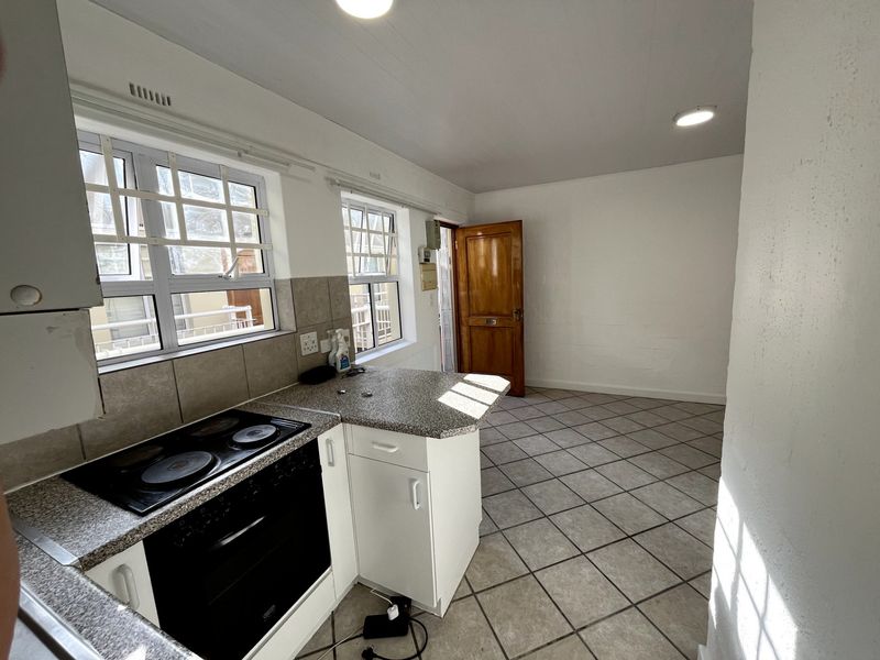 A functional, empty kitchen featuring built-in oven, electric hob, granite countertops, and tiled flooring, offering a blank canvas for potential renovation.