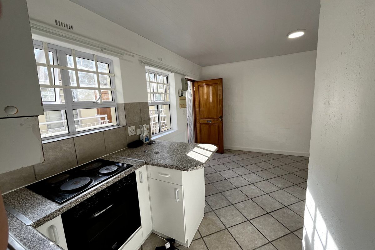 A functional, empty kitchen featuring built-in oven, electric hob, granite countertops, and tiled flooring, offering a blank canvas for potential renovation.