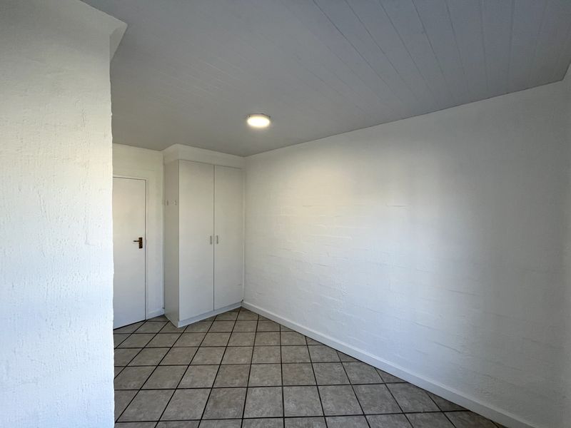 A clean, empty bedroom featuring tiled flooring, a built-in cupboard, and a neutral white finish, ready for personalization.