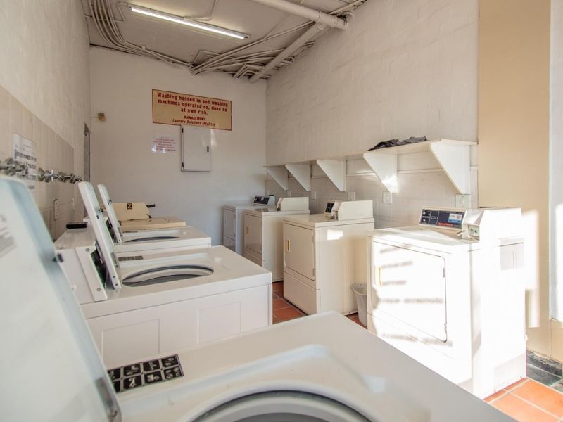 A functional communal laundry room featuring multiple washing machines and dryers, tiled flooring, and wall-mounted shelving for storage.