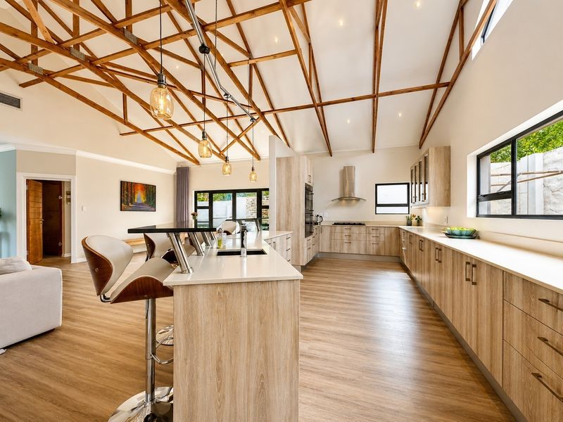 Spacious open-plan kitchen and living area featuring high vaulted ceilings with exposed timber trusses, modern cabinetry, and a large central island.