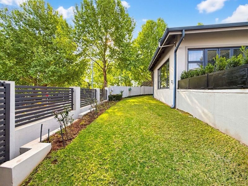 A well-maintained rear garden featuring a manicured lawn, modern slatted metal boundary fencing, and a concrete retaining wall alongside the house exterior.