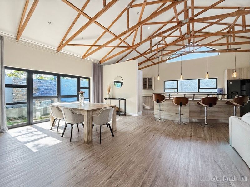 Spacious open-plan living and dining area featuring high vaulted ceilings with exposed timber trusses, modern kitchen island, and large sliding doors leading outdoors.