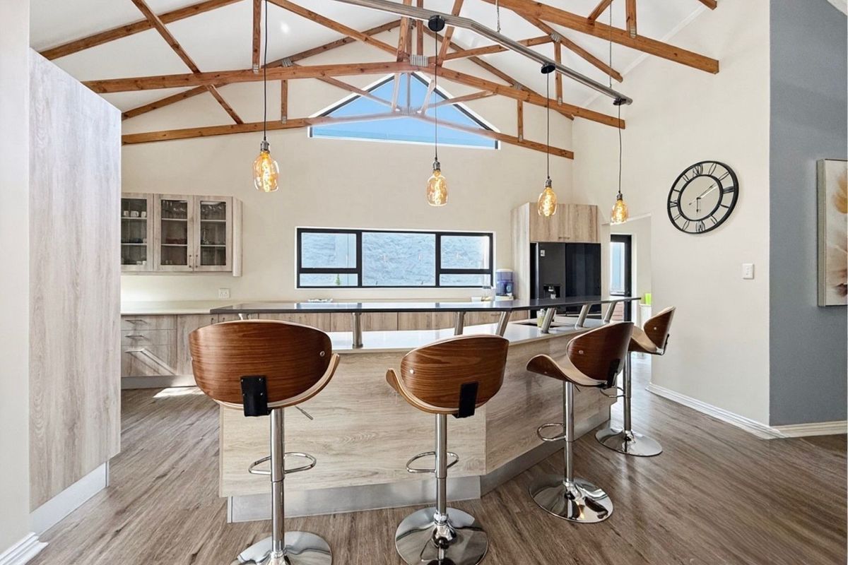 Modern kitchen featuring a large island, light wood-look cabinetry, and striking exposed timber roof trusses with high vaulted ceilings.