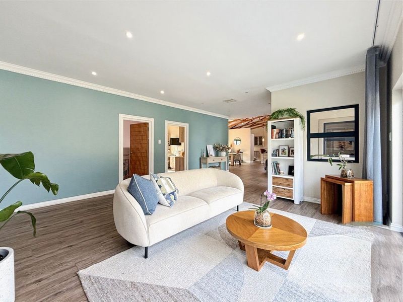 A bright and spacious living room featuring modern laminate flooring, recessed downlights, and elegant crown molding, creating a welcoming and well-maintained living space.