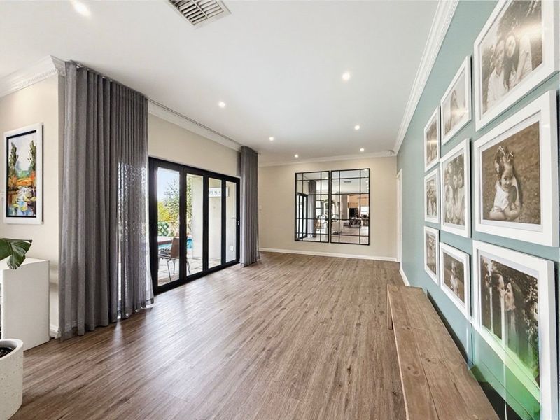Spacious living area featuring modern laminate flooring, recessed downlights, and bi-fold glass doors providing seamless access to the outdoor patio area.