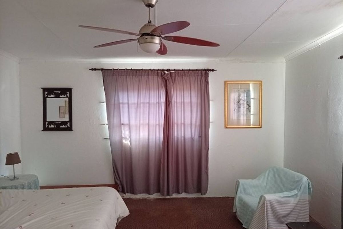 A bedroom featuring a ceiling fan and window with curtain rod, offering a functional space with neutral wall finishes.