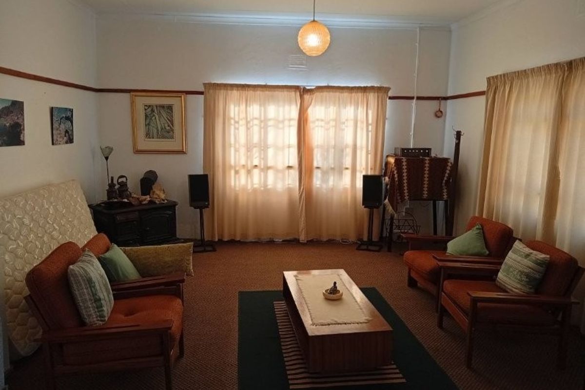 A traditional living room featuring carpeted flooring, neutral walls with picture rails, and natural light filtered through window curtains.