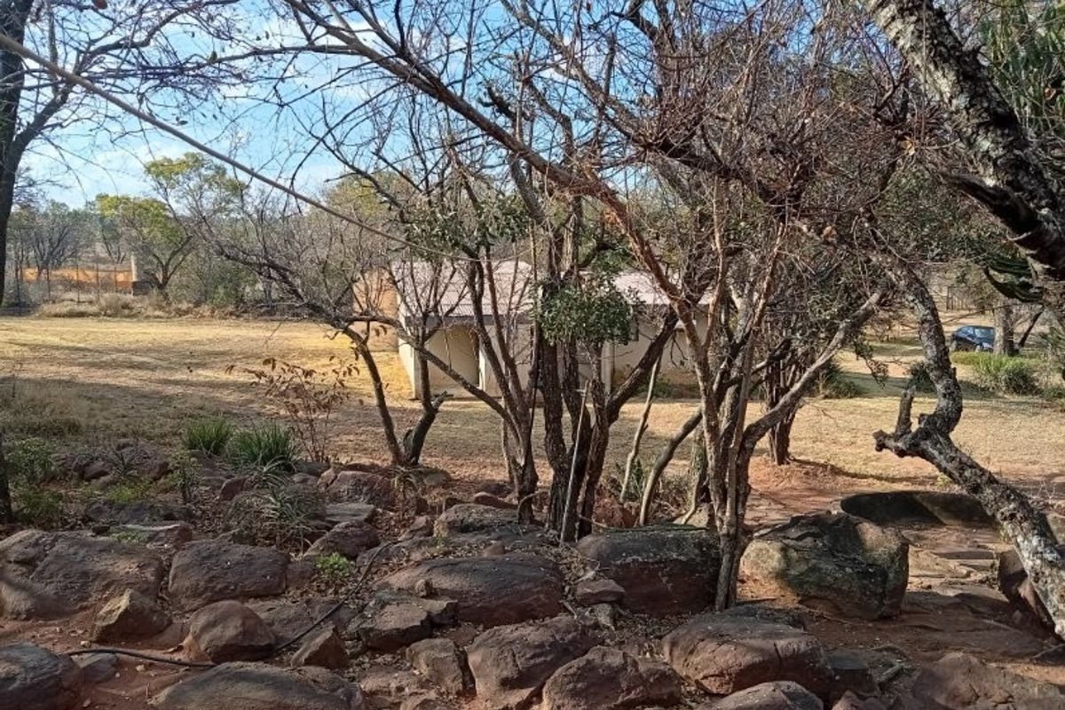 A view of the rear farm grounds featuring natural rocky terrain, mature trees, and a glimpse of the building structure with a metal roof.