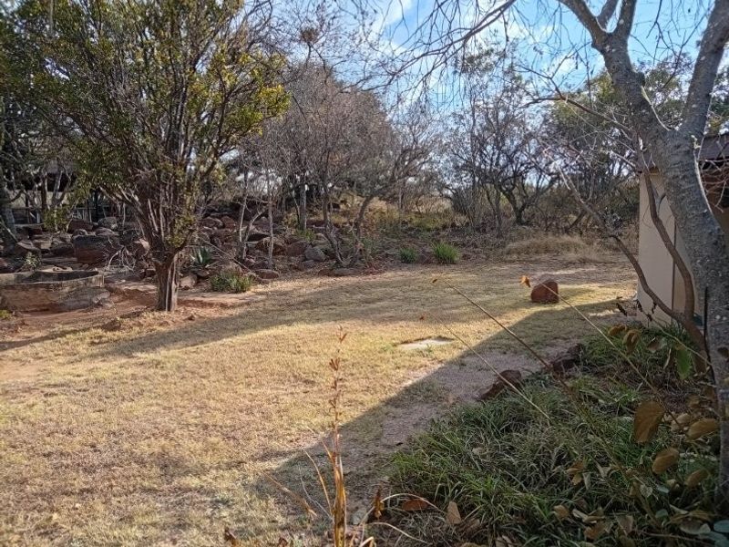 A natural, rustic garden area featuring mature trees, rocky terrain, and established vegetation, typical of a rural farm property setting.