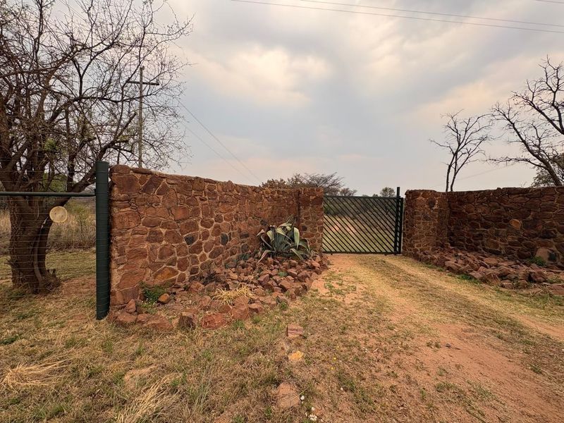 A rustic farm entrance featuring a stone boundary wall and a metal gate, providing secure access to the property grounds.