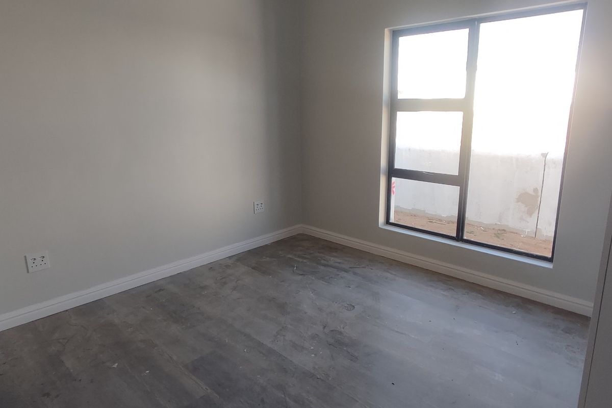 An empty bedroom featuring neutral walls, modern aluminium window frames, and unfinished flooring, offering a blank canvas for custom interior design.