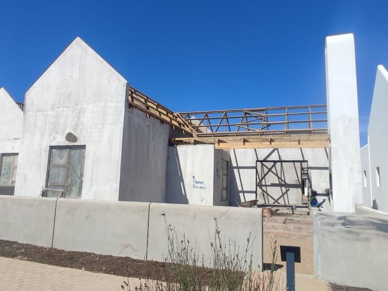 A residential property currently under construction, featuring unfinished exterior walls, exposed roof trusses, and installed solar panels on the completed section.