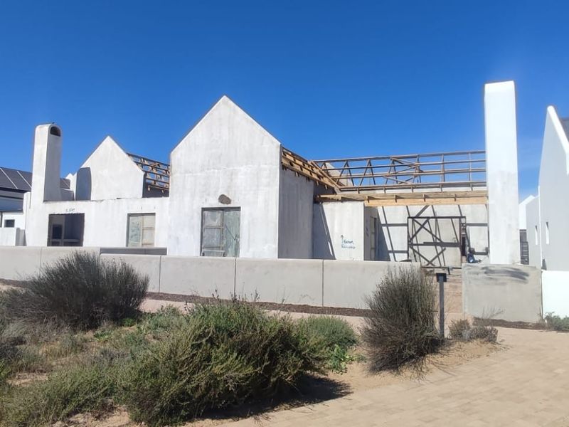 Front view of a residential property currently under construction, featuring exposed roof framing, unfinished exterior walls, and solar panels on adjacent completed sections.