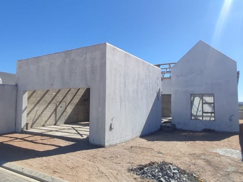 A residential property under construction, featuring a garage structure and main building shell with plastered walls and installed window frames.