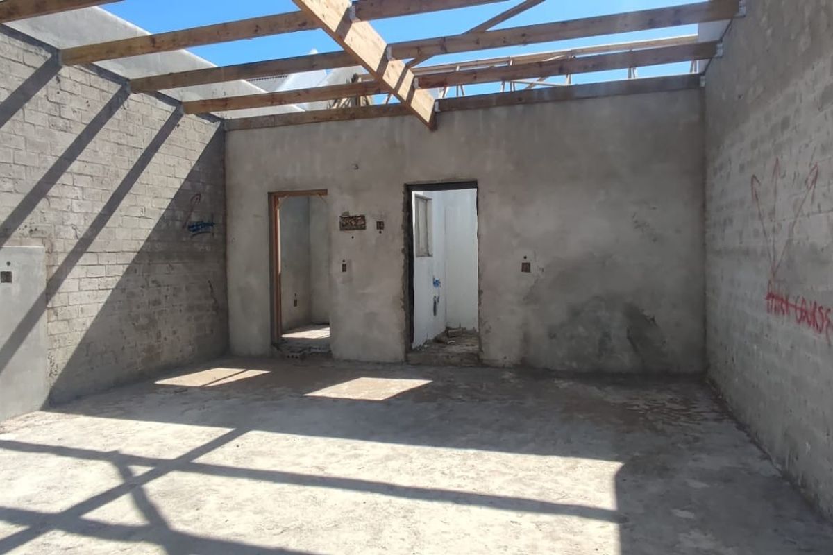 An unfinished interior space featuring exposed timber roof trusses, concrete block walls, and cement flooring, currently in a shell construction state.