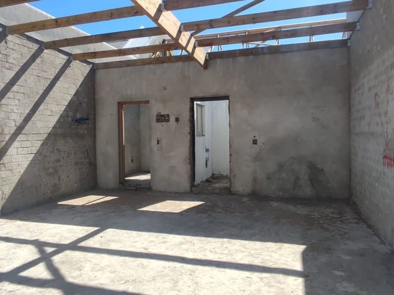 An unfinished interior space featuring exposed timber roof trusses, concrete block walls, and cement flooring, currently in a shell construction state.