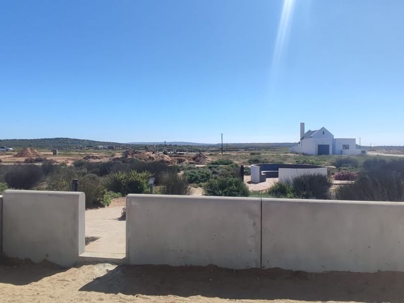 An elevated view overlooking a coastal landscape with natural vegetation and distant structures, framed by a modern concrete boundary wall.