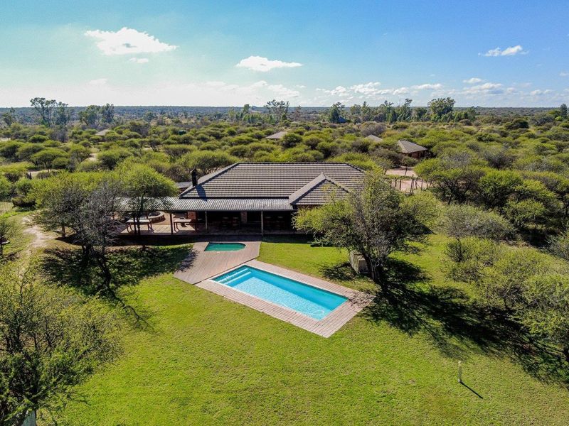Aerial view of a farm property featuring a swimming pool, wooden decking, and a covered patio set within a spacious, well-maintained garden landscape.
