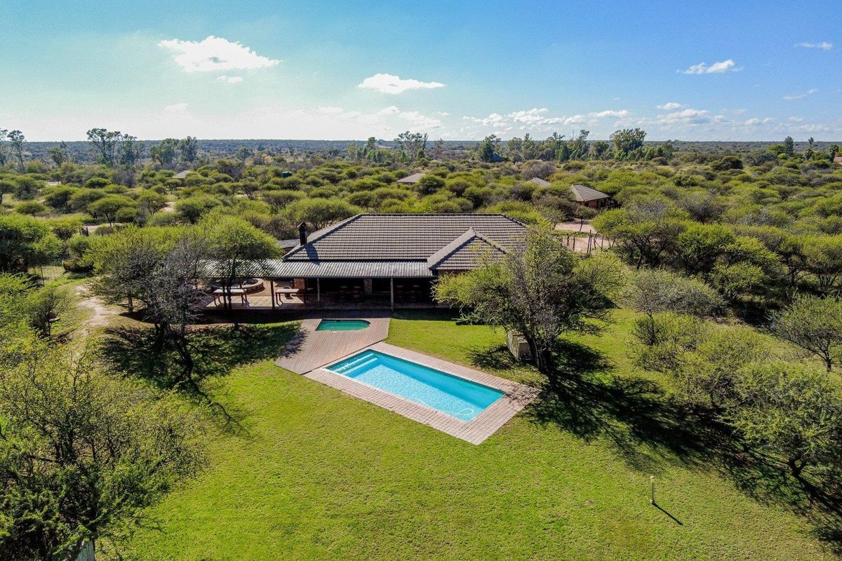 Aerial view of a farm property featuring a swimming pool, wooden decking, and a covered patio set within a spacious, well-maintained garden landscape.