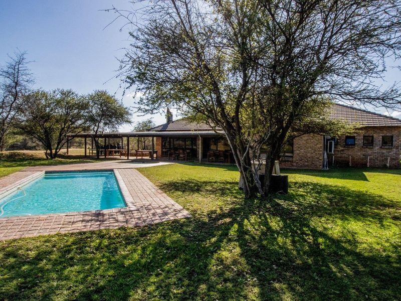 A spacious outdoor area featuring a swimming pool with brick paving, a covered patio, and a well-maintained garden setting on the farm property.