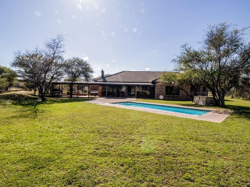 Rear view of the farm property featuring a swimming pool, wooden decking, and a spacious covered patio area set within a large garden.