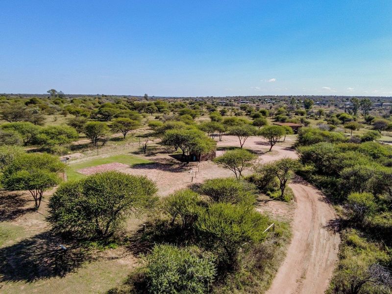 An aerial view of a large, open farm property featuring natural bushveld vegetation, a dirt access road, and scattered small structures.