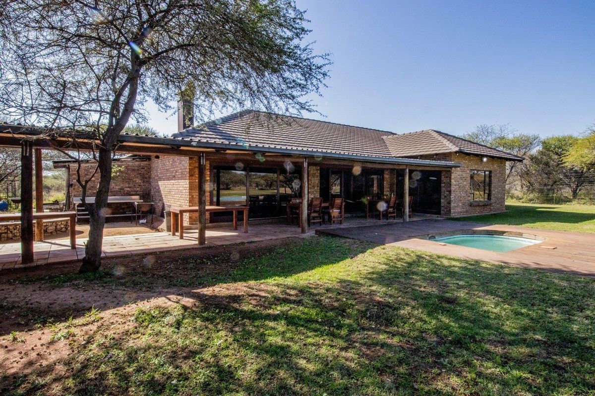 Rear view of a brick farmhouse featuring a covered patio, wooden decking, and a swimming pool set within a spacious garden.