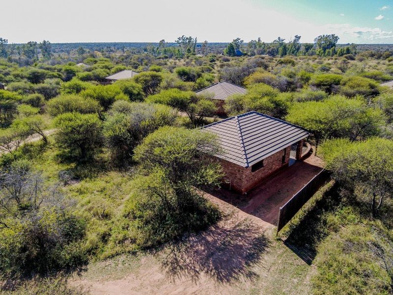 Aerial view of a brick farm dwelling with a tiled roof, situated within a natural bushveld landscape.