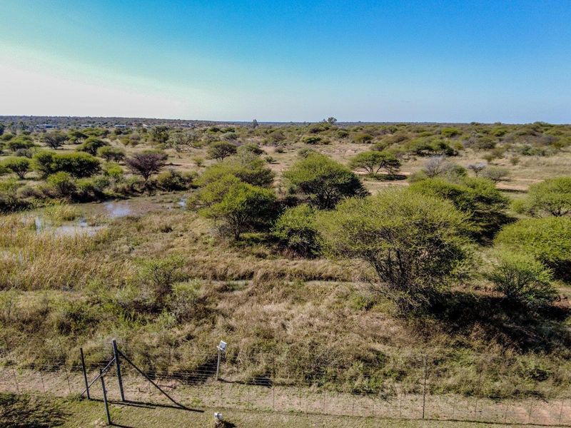 An aerial view of the expansive farm landscape featuring natural vegetation, open fields, and perimeter wire fencing under a clear blue sky.