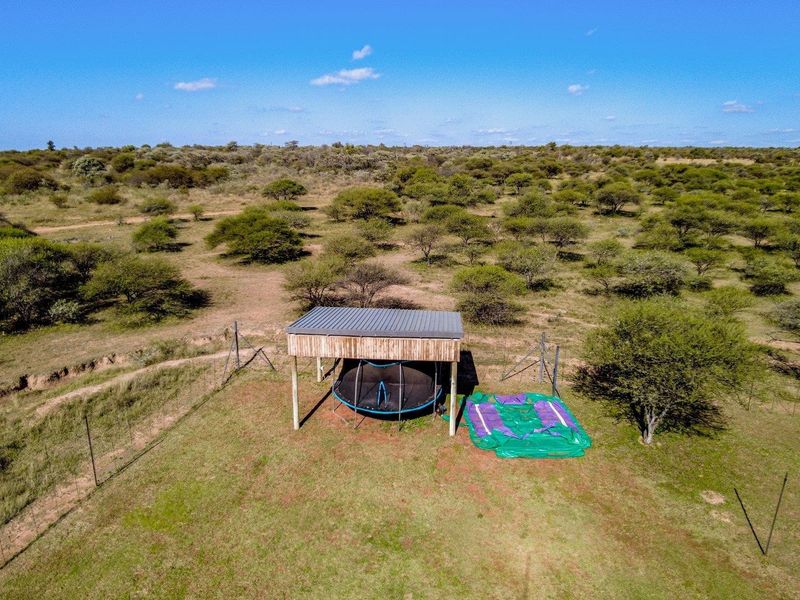 Aerial view of a rural property featuring a covered outdoor structure set within a large, open landscape with natural vegetation and perimeter fencing.