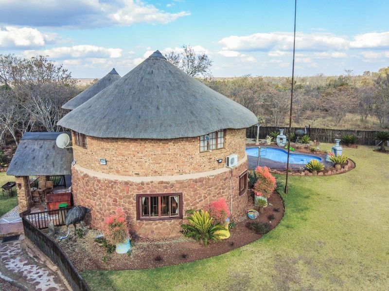 Aerial view of a circular farm dwelling featuring traditional thatch roofing, stone and brick exterior walls, and an adjacent swimming pool in a rural setting.