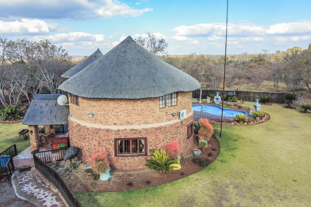 Aerial view of a circular farm dwelling featuring traditional thatch roofing, stone and brick exterior walls, and an adjacent swimming pool in a rural setting.