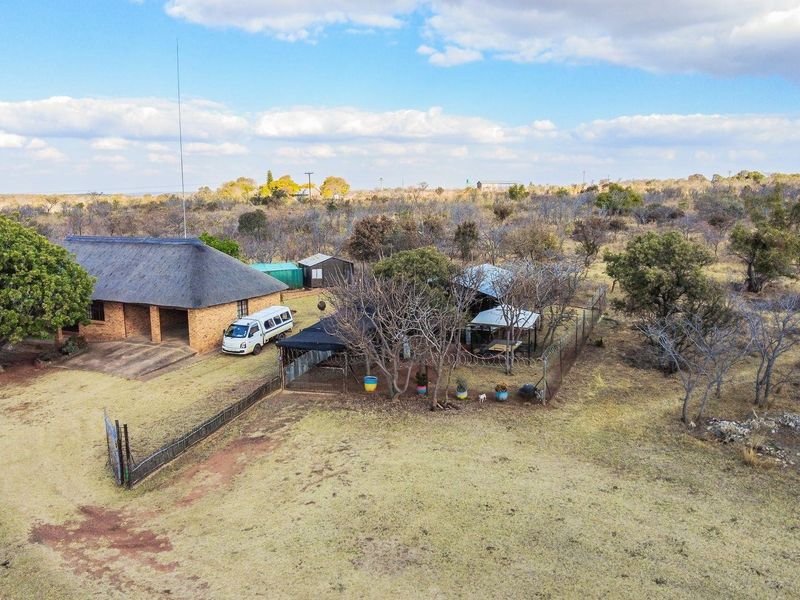 Aerial view of a farm property featuring a main house with a thatch roof, surrounding outbuildings, and expansive open land.