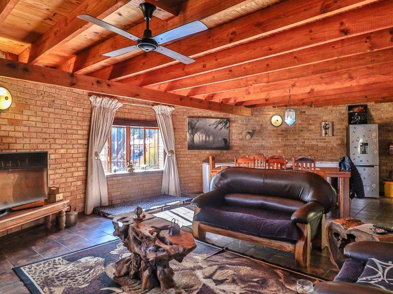 Spacious open-plan living area featuring rustic face brick walls, exposed timber beam ceilings, and tiled flooring, creating a warm and inviting atmosphere.