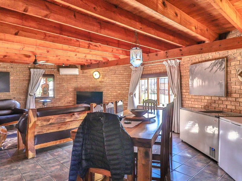 Spacious open-plan living and dining area featuring rustic face brick walls, exposed timber beam ceilings, and durable tiled flooring.