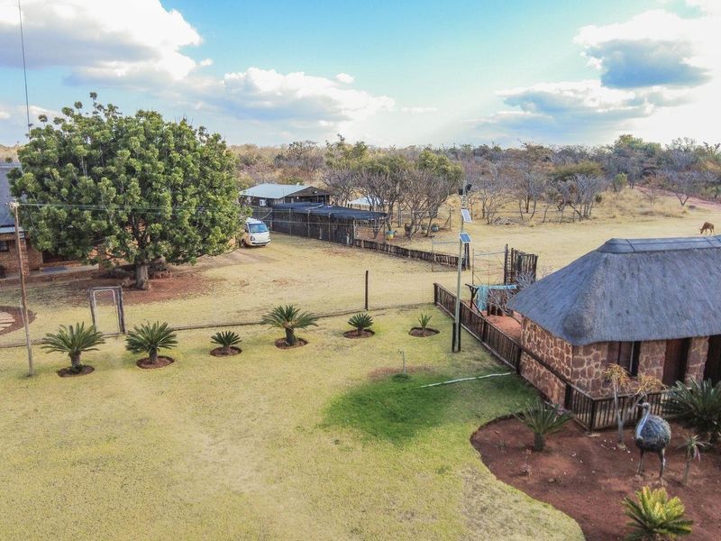 Aerial view of a farm property featuring multiple structures with traditional thatch roofs, stone masonry, and expansive landscaped grounds.