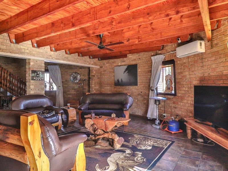 Rustic living room featuring exposed timber beam ceilings, face brick walls, tiled flooring, and a split-system air conditioner.