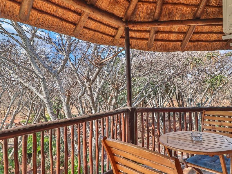 A covered outdoor patio featuring a traditional thatch roof and timber railing, offering scenic views of the surrounding natural landscape.