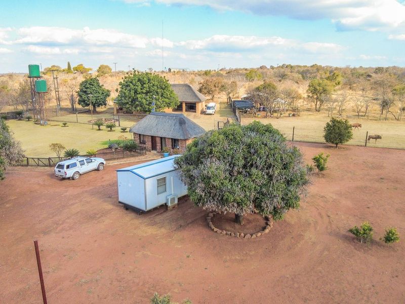 Aerial view of a farm property featuring multiple structures, including thatched roof buildings, water tanks, and fenced grounds in a rural landscape.