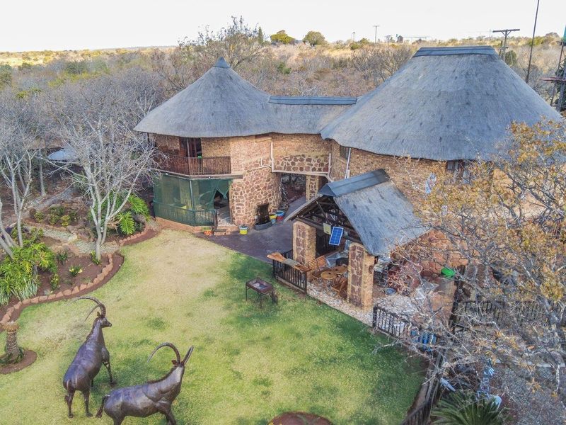 Aerial view of a rustic farm property featuring traditional thatched roofs, stone construction, a covered patio area, and elevated water storage tanks.