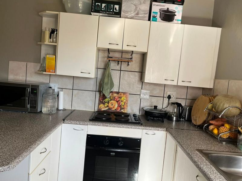 A functional kitchen featuring white cabinetry, laminate countertops, a built-in oven with electric hob, and a tiled backsplash.