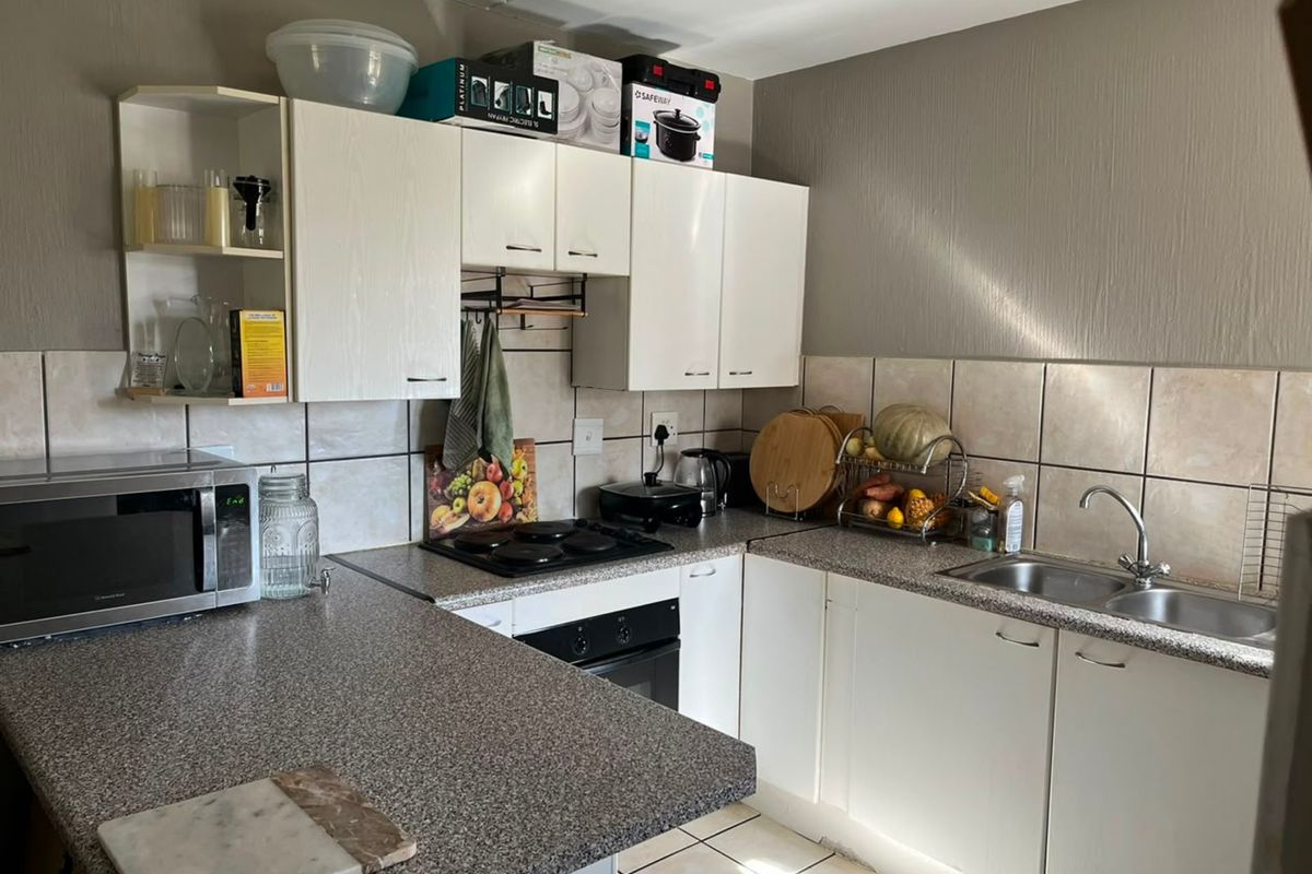 A functional kitchen featuring laminate countertops, built-in oven, electric hob, and stainless steel double sink with tiled backsplash and ample cabinetry.