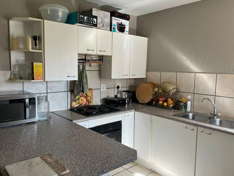 A functional kitchen featuring laminate countertops, built-in oven, electric hob, and stainless steel double sink with tiled backsplash and ample cabinetry.