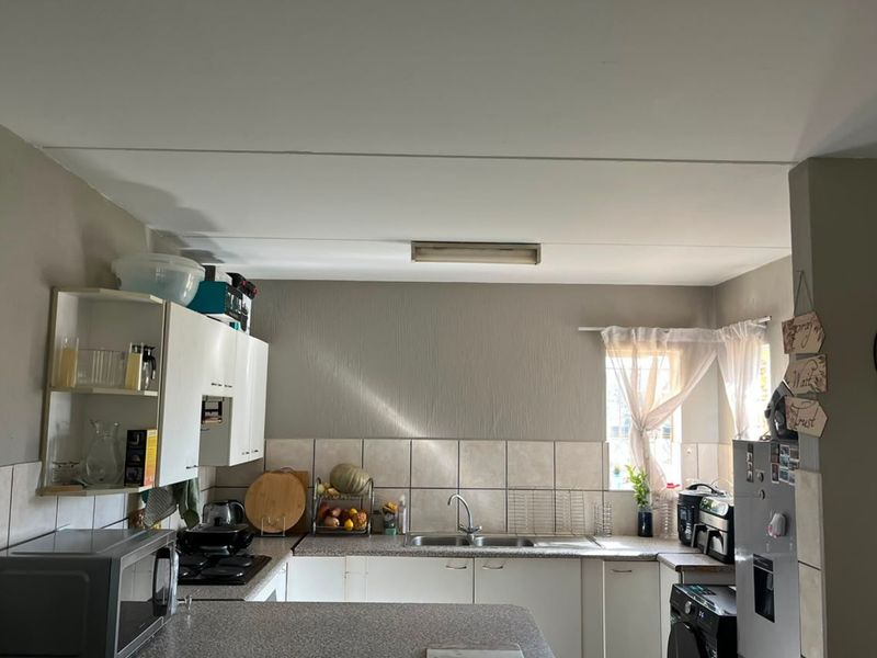 A functional kitchen featuring white cabinetry, laminate countertops, a tiled backsplash, and a stainless steel sink, with a window providing natural light.