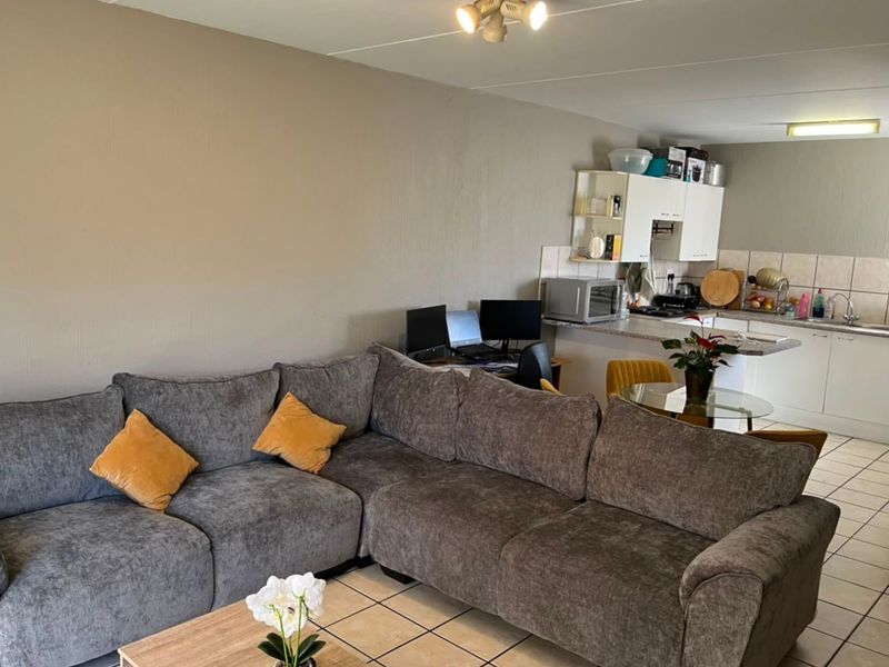 Open-plan living area featuring a functional kitchen with tiled flooring, cabinetry, and a breakfast counter, seamlessly connected to the lounge space.