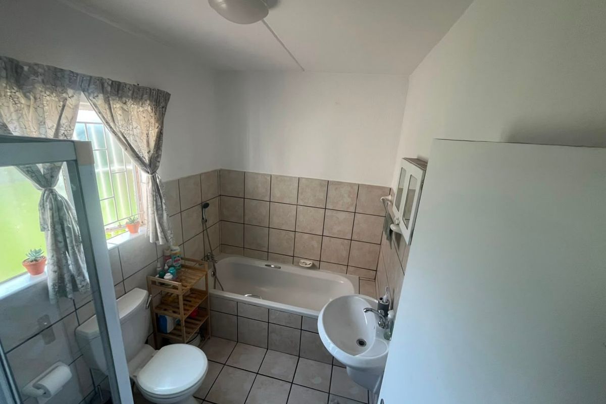 A functional bathroom featuring a bathtub, pedestal basin, toilet, and neutral wall and floor tiling, providing a practical layout for daily use.