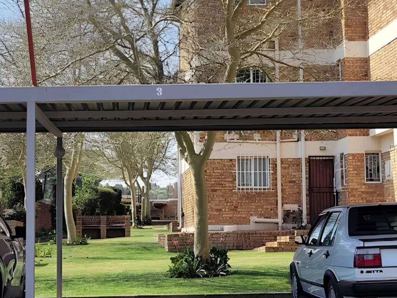 View of the apartment complex rear exterior featuring a covered carport, brick facade, and communal garden area.