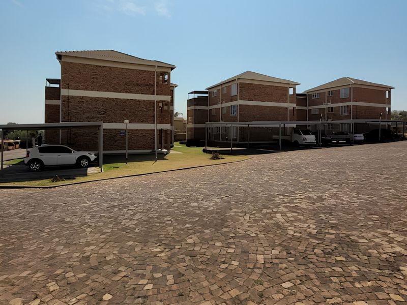 Exterior view of a multi-story apartment complex featuring brick facades, covered parking carports, and a paved driveway area.